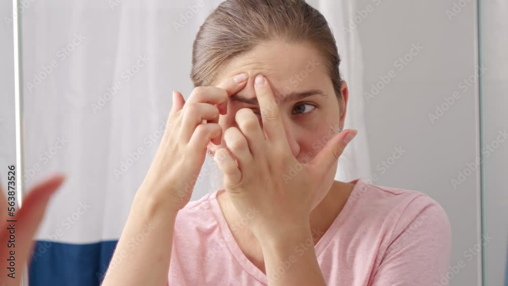 Beautiful young woman looking for pimples and squeezing them in bathroom. Concept of female aging, skin issues, facial treatment and care Beautiful young woman looking for pimples and squeezing them in bathroom. Concept of female aging, skin issues, facial treatment and care