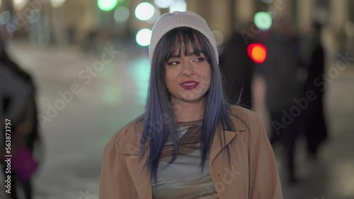 medium shot of a very confident young girl with the background out of focus with people and vehicles passing behind at night