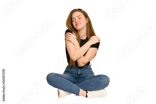 Young redhead woman sitting on the floor cut out isolated hugs, smiling carefree and happy.