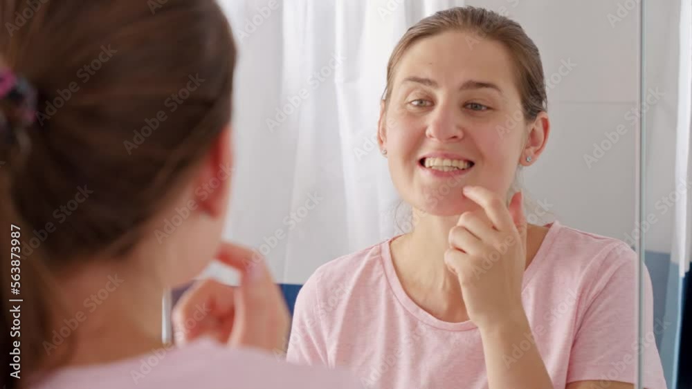 Portrait of smiling young woman opens mouth and looks at the reflection of her teeth in mirror. Concept of teeth health, self checking mouth and oral hygiene Portrait of smiling young woman opens mouth and looks at the reflection of her teeth in mirror. Concept of teeth health, self checking mouth and oral hygiene