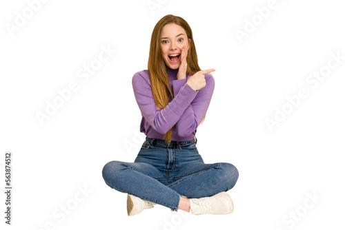 Young redhead woman sitting on the floor cut out isolated laughs joyfully keeping hands on head. Happiness concept.