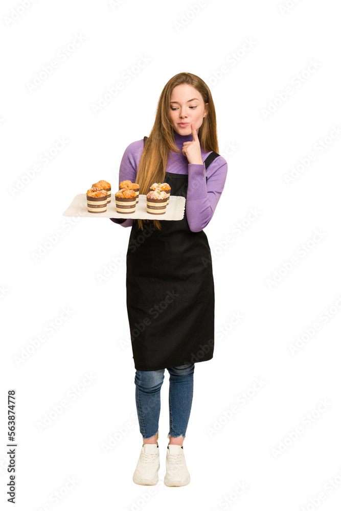Full body of a young redhead woman holding a recently made muffins cut out isolated Full body of a young redhead woman holding a recently made muffins cut out isolated