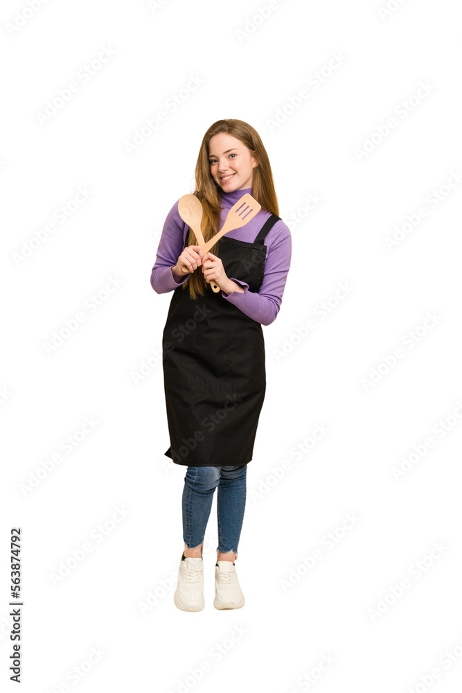 Young novice redhead woman with apron and wooden spoon and fork cut out isolated Young novice redhead woman with apron and wooden spoon and fork cut out isolated