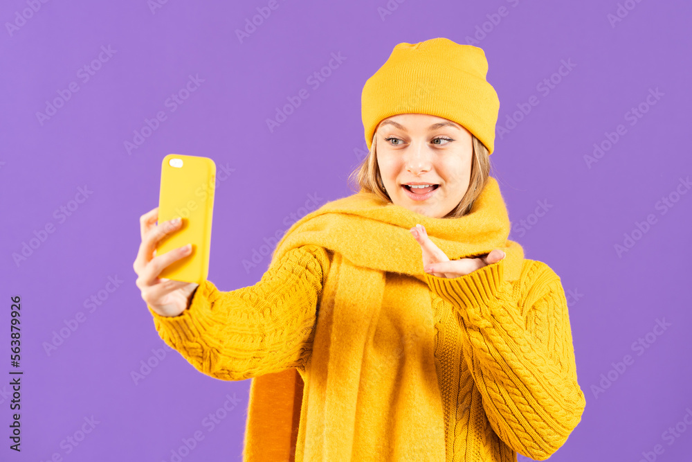Young woman on winter clothes live streaming or having video call on phone isolated on purple background