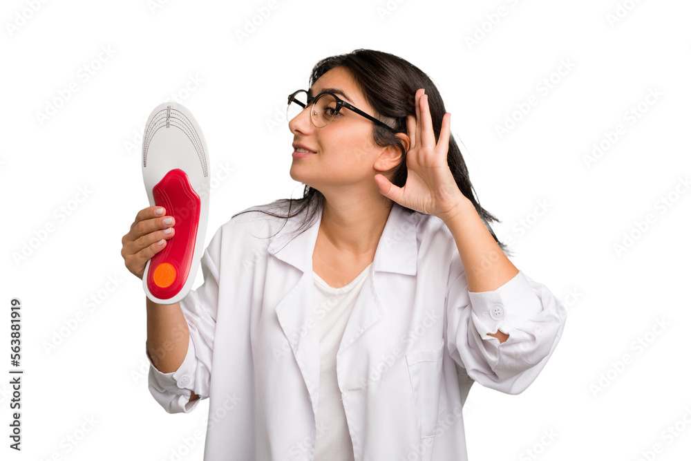 Young indian chiropodist woman holding a insoles for shoes cut out isolated trying to listening a gossip. Young indian chiropodist woman holding a insoles for shoes cut out isolated trying to listening a gossip.