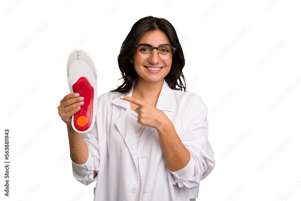 Young indian chiropodist woman holding a insoles for shoes cut out isolated smiling and pointing aside, showing something at blank space. Young indian chiropodist woman holding a insoles for shoes cut out isolated smiling and pointing aside, showing something at blank space.
