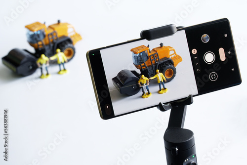 Smartphone on a gimbal selfie stick for photo-video, filming toy construction machinery and workers. Concept of live broadcast construction, video blogging, podcasts, streaming and journalism.