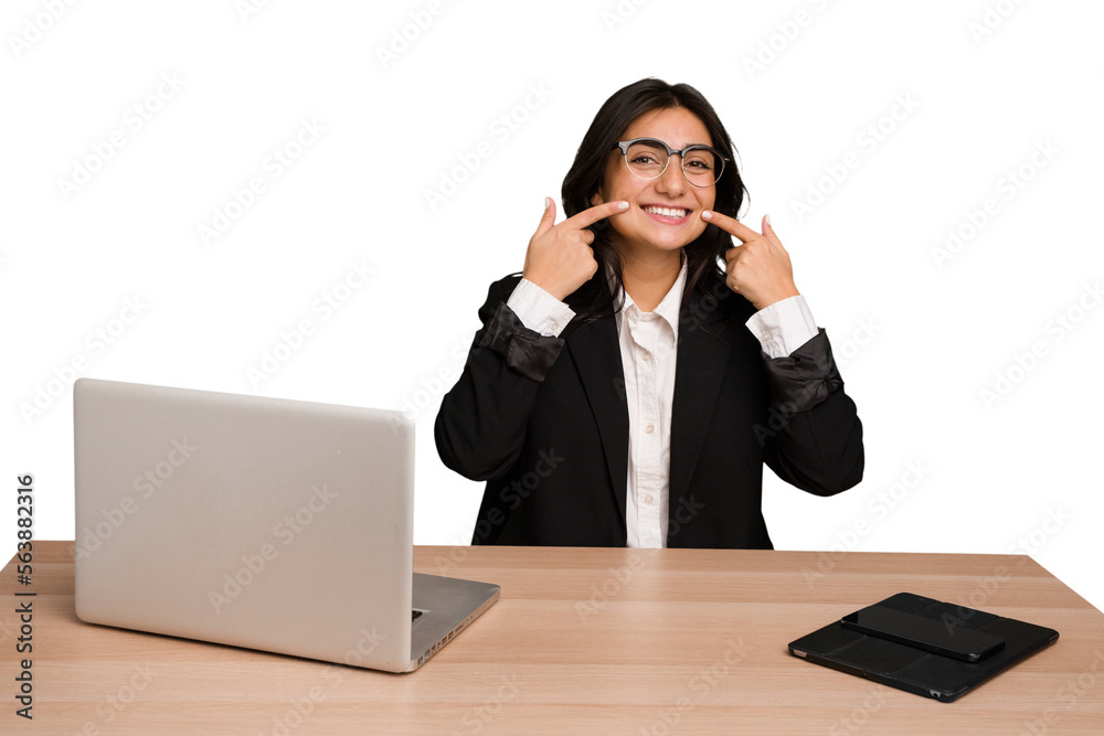 Young indian woman in a table with a laptop and tablet isolated smiles, pointing fingers at mouth. Young indian woman in a table with a laptop and tablet isolated smiles, pointing fingers at mouth.