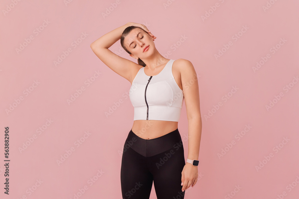 Obraz premium Sport concept. Young caucasian woman doing exercises while standing on pink background. Studio portrait of attractive girl wearing sportswear posing over pink background