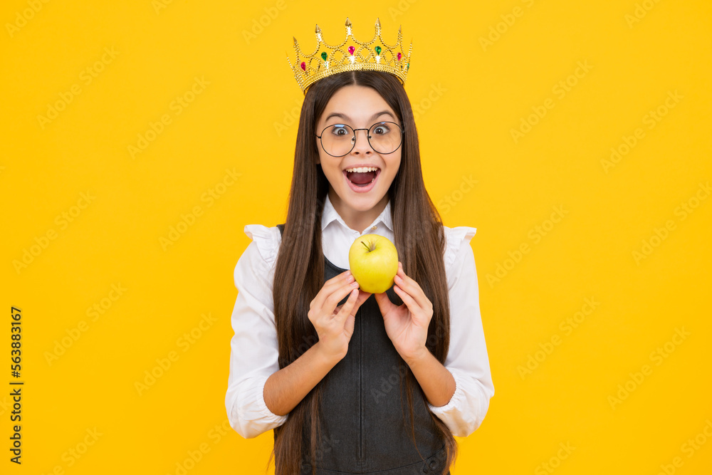 Teen child in queen crown hold apple isolated on yellow background. Princess girl in tiara. Teenage girl wear diadem. Excited face, cheerful emotions of teenager girl.