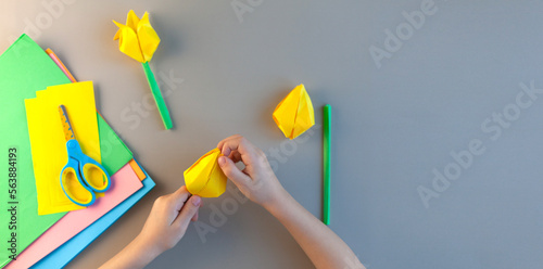 Close-up of the hands of a small child makes yellow tulips of paper for mom for mother's day or on March 8 or birthday. A simple pleasant idea of a children's gift to mom.