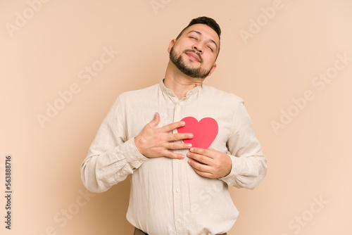 Adult latin man holding a paper heart, valentines day concept isolated