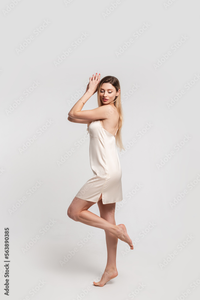 Happy beautiful woman with a smile with a slim body in a fashionable beige nightgown poses in the studio
