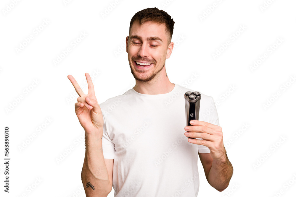 Young man holding a shaving machine cut out isolated joyful and carefree showing a peace symbol with fingers. Young man holding a shaving machine cut out isolated joyful and carefree showing a peace symbol with fingers.