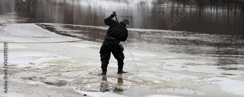 Lifeguard diver saws ice on the river with a big hand saw at winter day photo