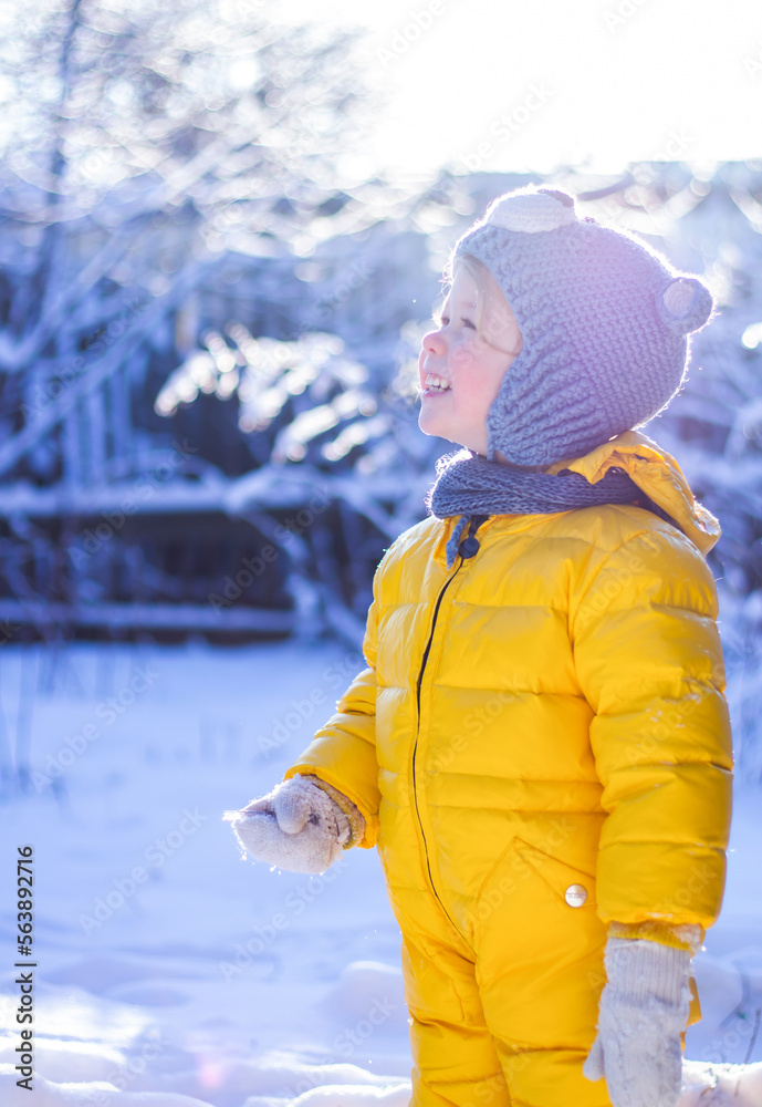 Portrait of smiling little child girl in blue hat and yellow snowsuit  playing in snow on sunny winter day