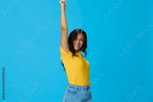 Woman in yellow t-shirt on blue background posing gestures emotions and signals with smile, hands up happiness copy space