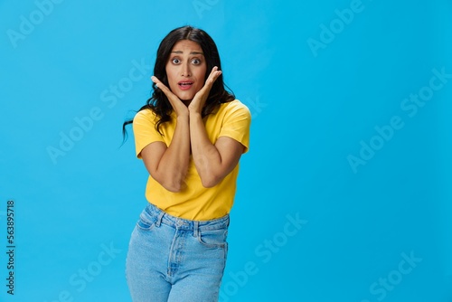 Woman in yellow t-shirt on blue background posing gestures emotions and signals with smile, hands up happiness copy space