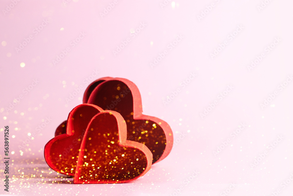 Red hearts on pink background with golden particles for festive image with copy space.