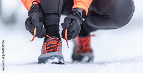 An attractive female runner is tying her shoelaces before training on the snow in the winter season.