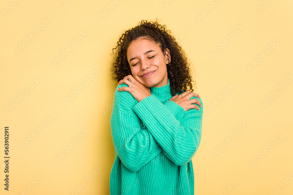 Young Brazilian curly hair cute woman isolated on yellow background hugs, smiling carefree and happy. Young Brazilian curly hair cute woman isolated on yellow background hugs, smiling carefree and happy.