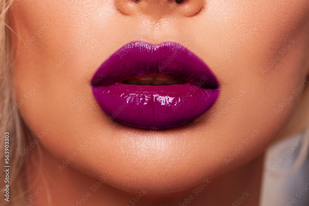 Obraz premium Close-up Beautiful woman lips. makeup. Lip glossy lipstick. Sexy lips. Part of face, young woman close up. cherry or purple color lipstick on large lips. Perfect beautiful makeup. 