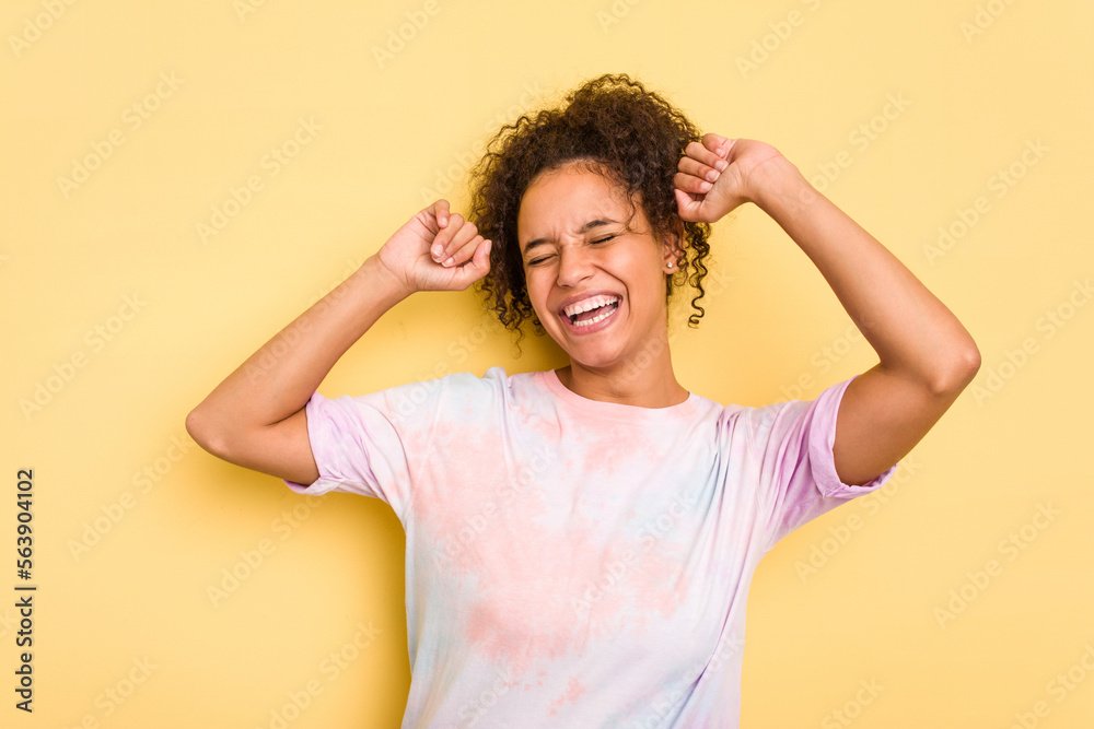 Young Brazilian curly hair cute woman isolated on yellow background celebrating a special day, jumps and raise arms with energy. Young Brazilian curly hair cute woman isolated on yellow background celebrating a special day, jumps and raise arms with energy.