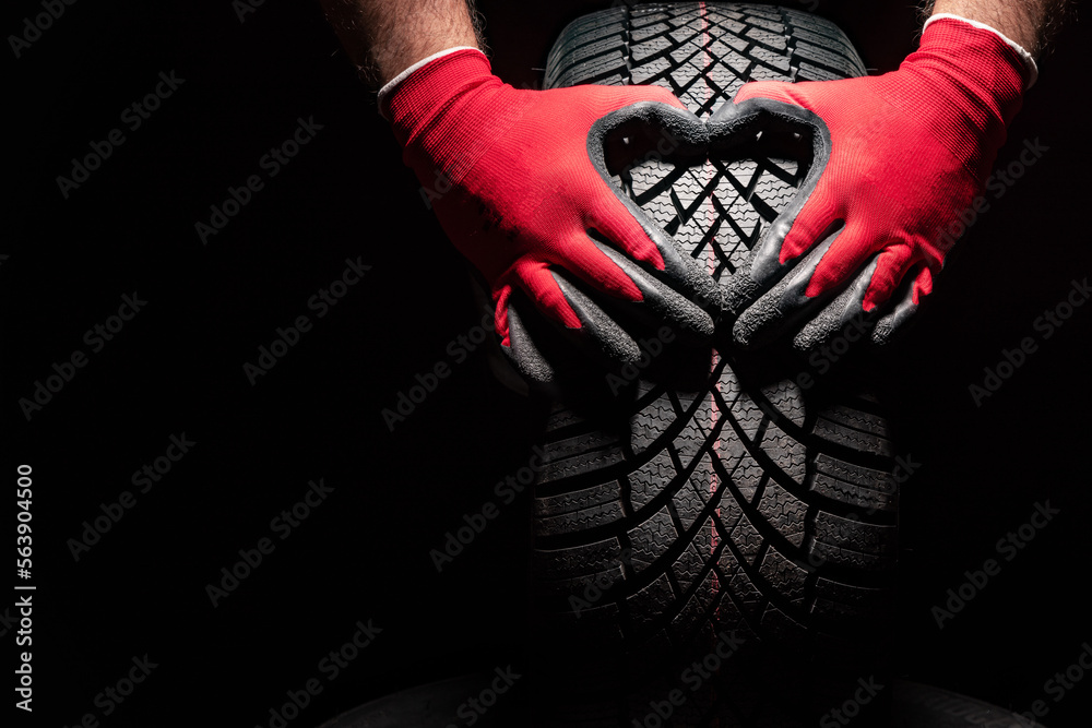 Car tire service and hands of mechanic holding new tyre on black background with copy space for text - obrazy, fototapety, plakaty 
