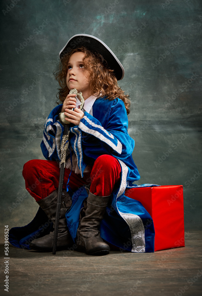 Emotional kid, little girl wearing costume of prince, musketeer and royal person posing over dark vintage style background. Fashion, theater, beauty, emotions concept Emotional kid, little girl wearing costume of prince, musketeer and royal person posing over dark vintage style background. Fashion, theater, beauty, emotions concept