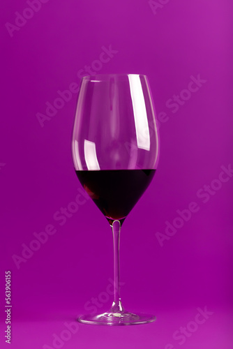 Elegant wine glass with tasty red wine on violet background
