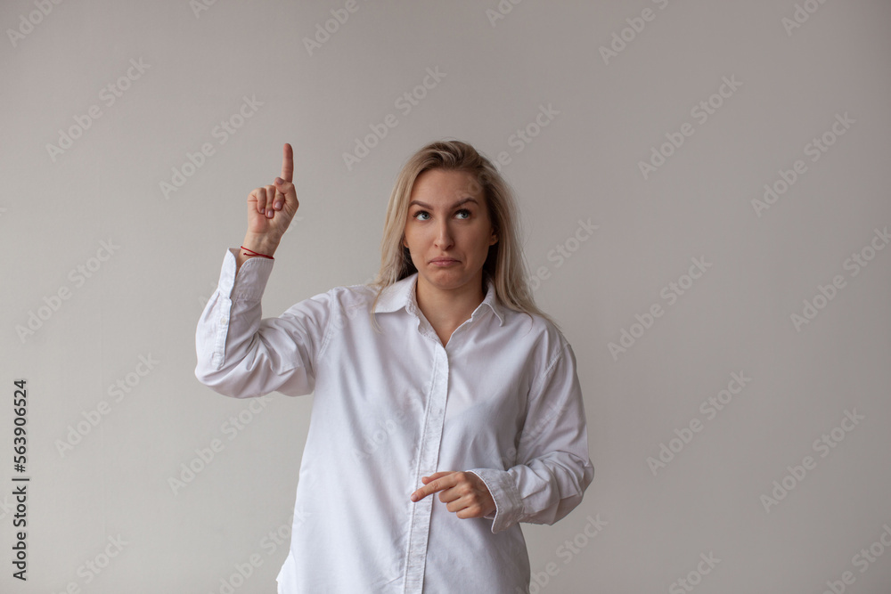 Fototapeta premium A young woman in a white shirt points up. White background.