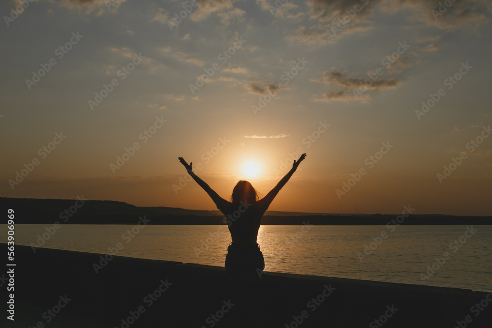 The silhouette of young sexy girl enjoying the sundown with raised up hands at the Italian lake beach 