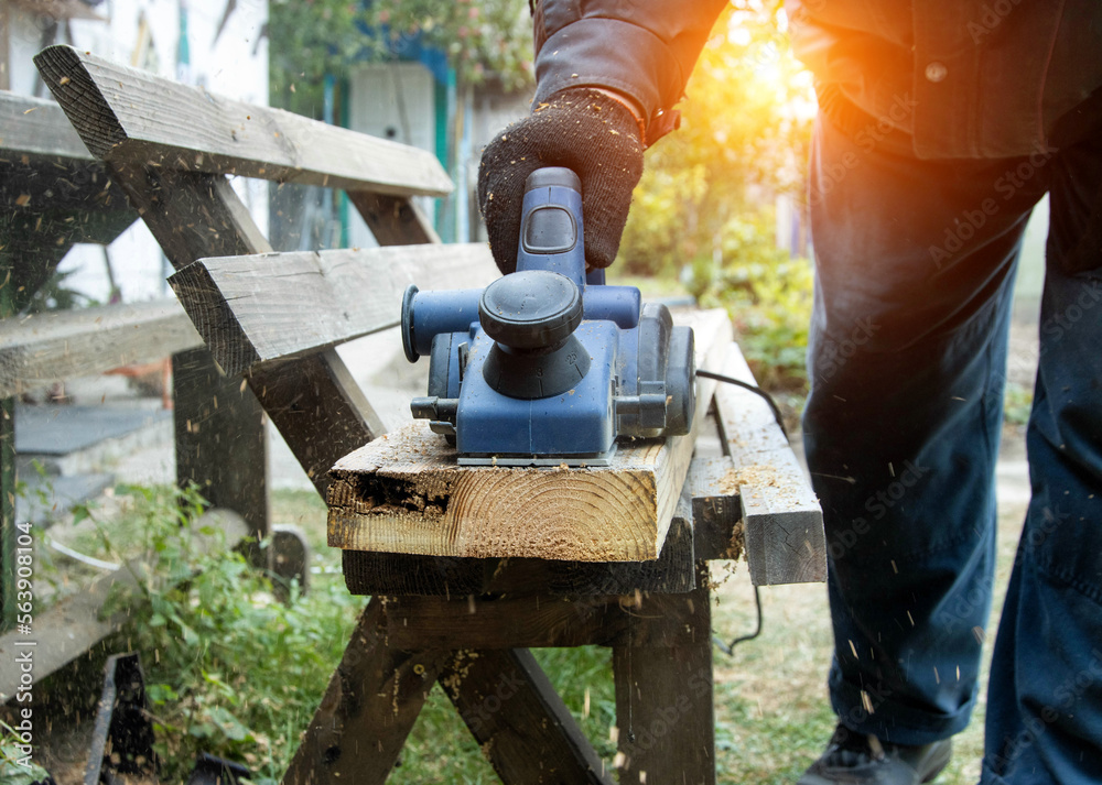 A man works with an electric tool with an electric planer, cleans old wood. Industry, sunset