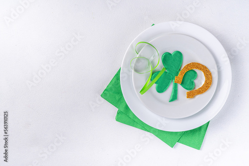 St. Patrick's Day festive table setting. Plate and cutlery with green napkin, shamrock symbol, gold horseshoe decor for luck. Patrick Day menu background, party invitation, top view copy space