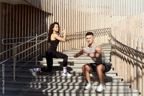 Fit couple doing squats on city street stairs with focused faces