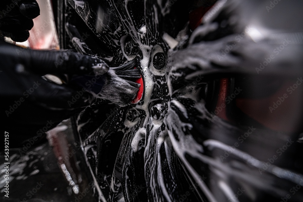 Employee of a car detailing studio or a car wash thoroughly washes the aluminum rim of a sports car.