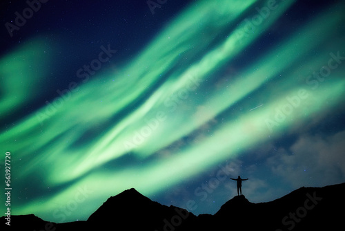 Mountaineer standing on top of mountain with Aurora Borealis glowing in the night sky on arctic circle © Mumemories