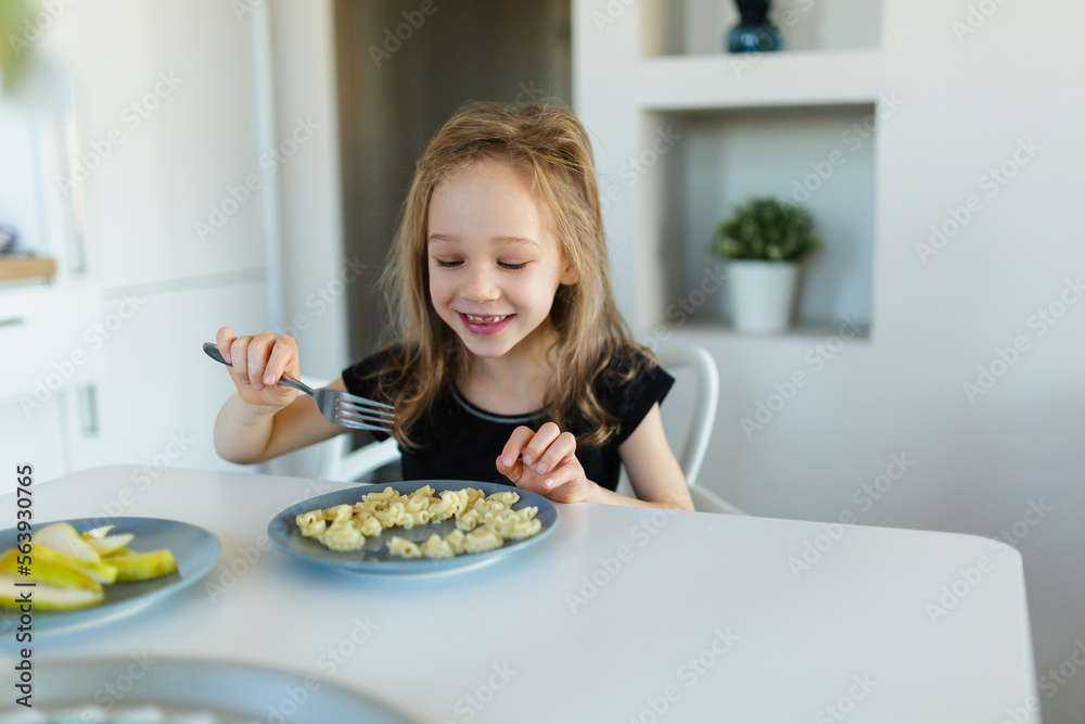 Happy preschool girl eating pasta at table Happy preschool girl eating pasta at table