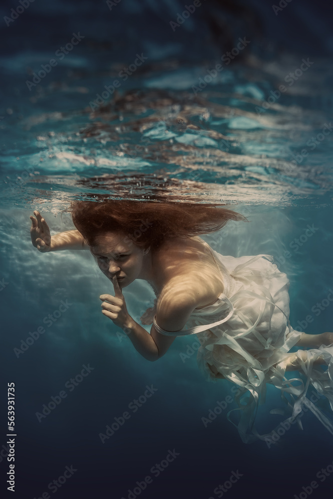 Portrait of a girl with long hair in a white dress with ribbons underwater