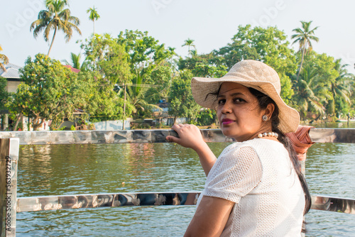 Fotografia Attractive and Happy woman or lady with hat enjoys her tropical vacation on backwater of alleppey or Alappuzha from Houseboat