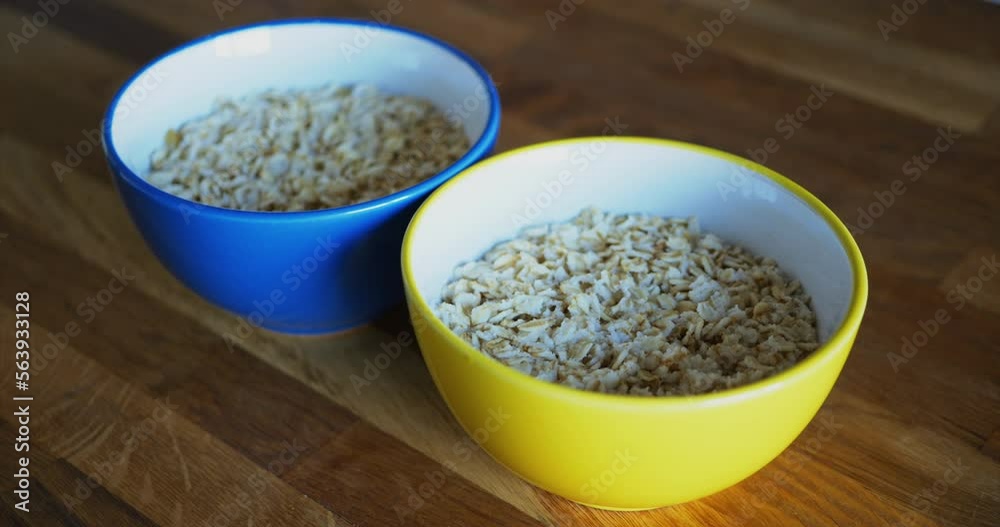 Oatmeal is a delicious and healthy natural breakfast. Close-up of two ceramic cups in blue and yellow, the colors of the Ukrainian flag, with oatmeal on a brown wooden table. Top side view Oatmeal is a delicious and healthy natural breakfast. Close-up of two ceramic cups in blue and yellow, the colors of the Ukrainian flag, with oatmeal on a brown wooden table. Top side view