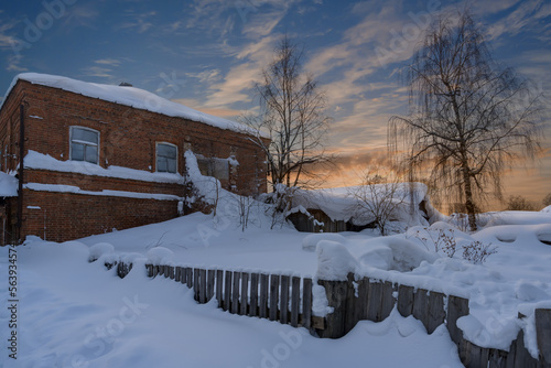 High snowdrifts wrapped a fluffy blanket around a wooden fence and an old brick house.