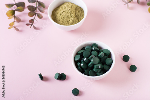 Detox and antioxidant. Matcha powder and spirulina pills in bowls on a pink background.