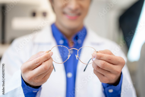 An optometrist in a white medical gown in an opticians salon holds round glasses for vision. Help in choosing eyeglasses. photo