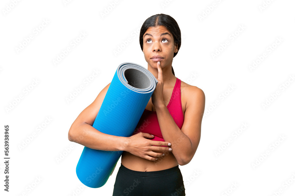 Young sport African American woman going to yoga classes while holding a mat over isolated background having doubts while looking up