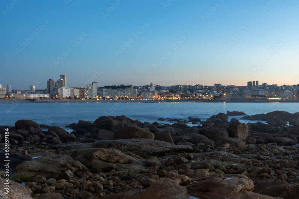 The rocky shore of the ocean, in the distance the evening city in illumination.