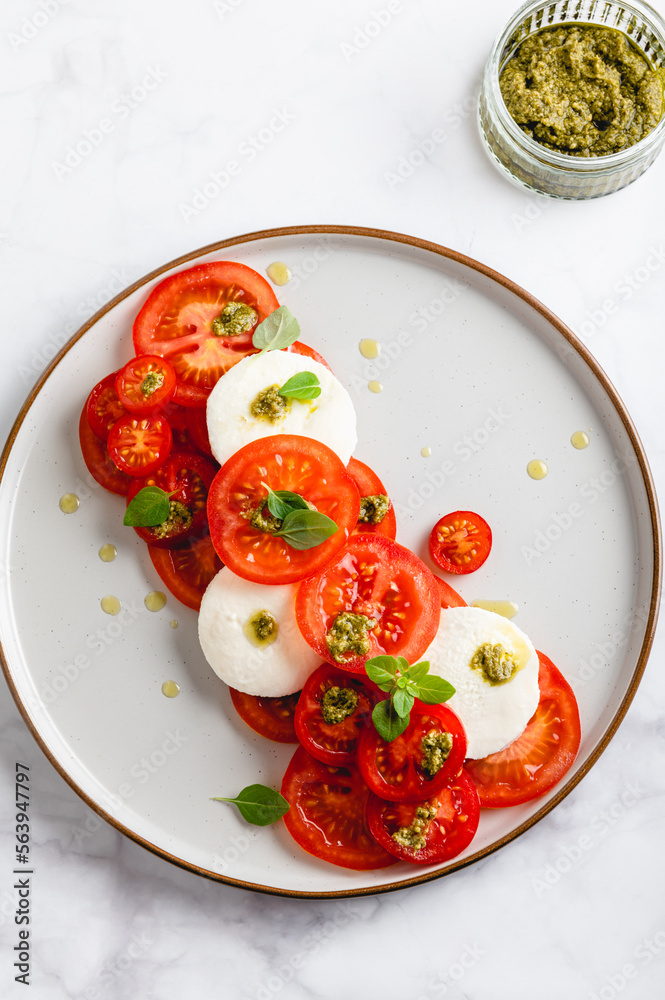 Classic italian salad caprese served in original form with different tomatoes, mozarella, pesto sauce and basil