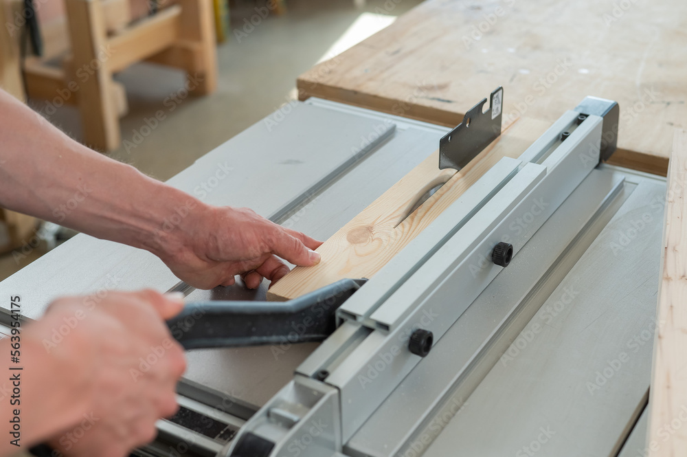 Close-up of a man cutting a wooden board on a sawing machine.
