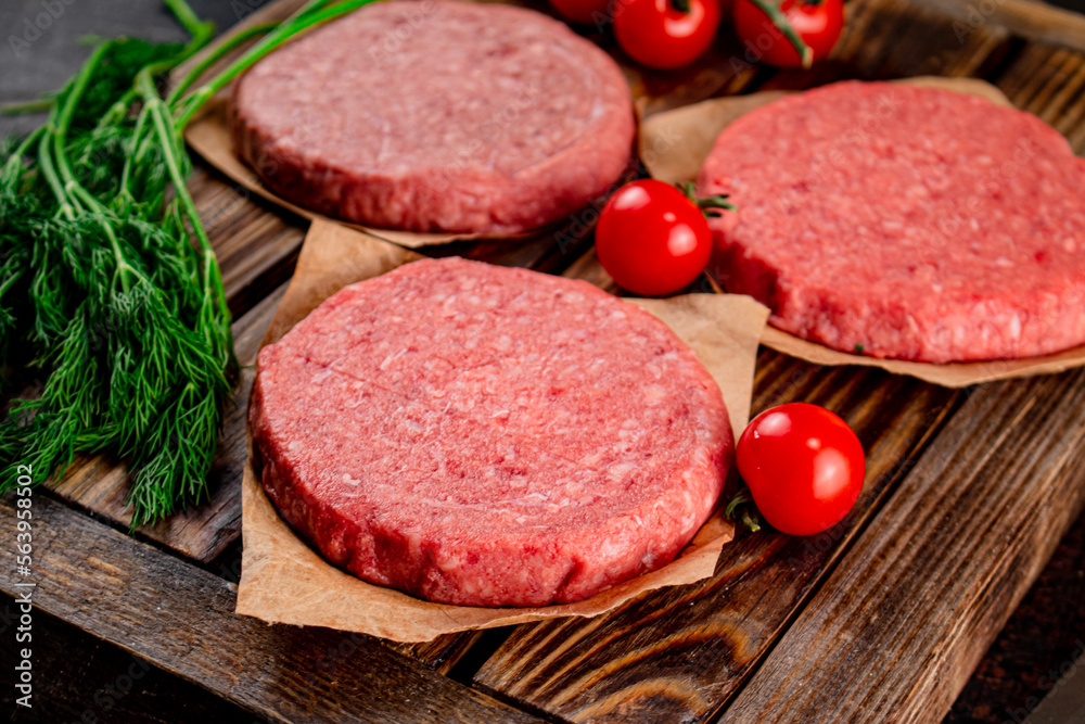 Raw burger on a wooden tray with tomatoes and dill. Raw burger on a wooden tray with tomatoes and dill.