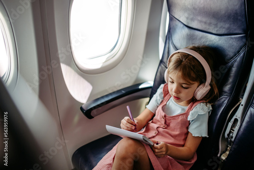 Little girl in airplane drawing and listening music.